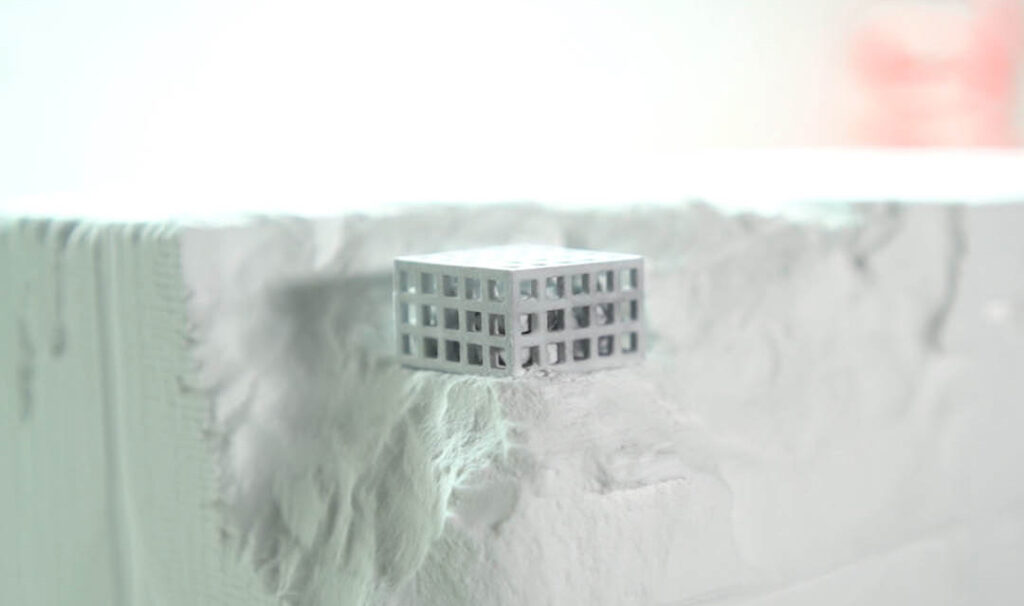 3D-printad detalj i form av en gitterkub placerad i återvunnet SLS/MJF-pulver, som illustrerar additiv tillverkning med hållbara material.